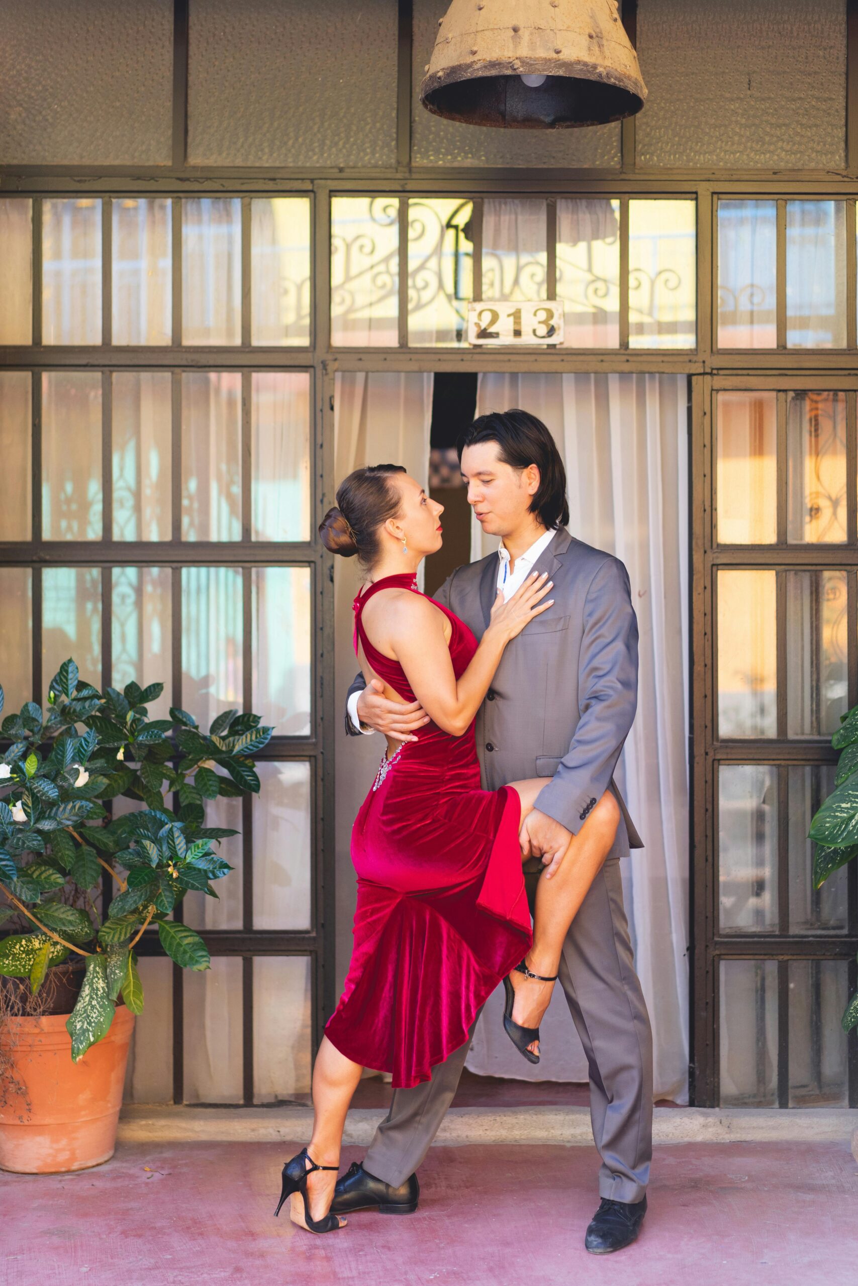 A couple gracefully dances tango outdoors in front of a charming building with potted plants.